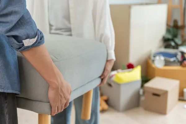 zwei Personen tragen einen Hocker, im Hintergrund stehen Umzugskartons