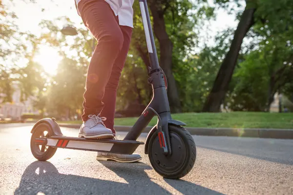 Eine Person steht mit auf einem E-Scooter im Park.