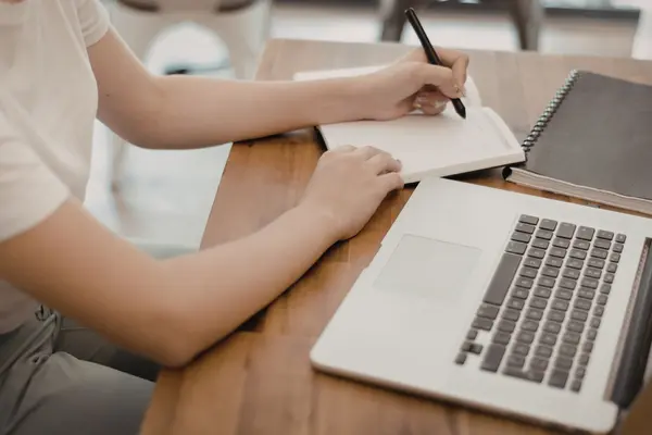 Person sitzt am Laptop und macht Notizen