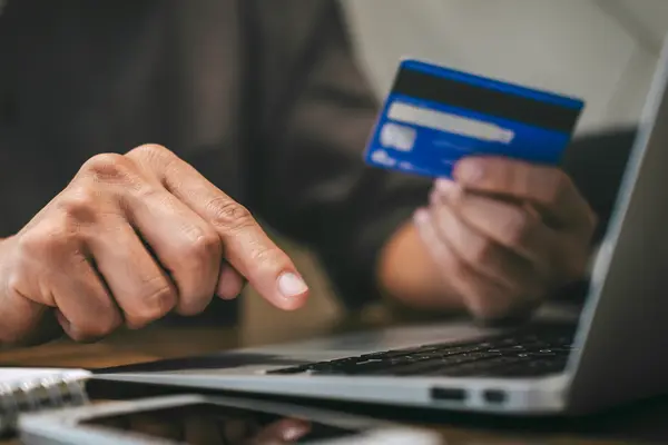 eine Person hält eine Kreditkarte in der Hand während sie vor einem Laptop sitzt
