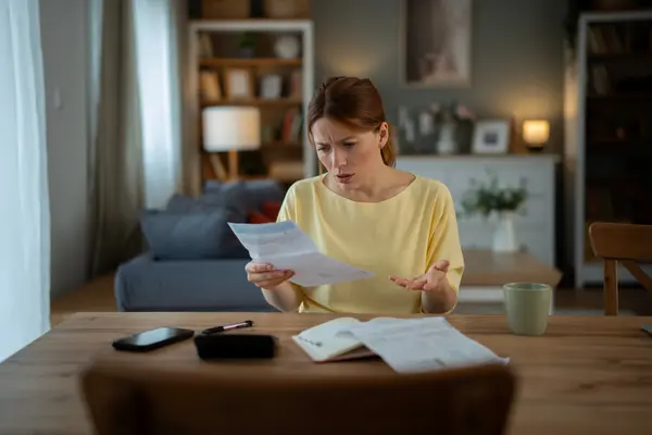 Frau im Wohnzimmer wundert sich über ein Schreiben.