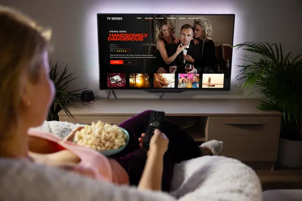 Frau schaut Serie über Streaming-Dienste mit Popocorn zuhause.