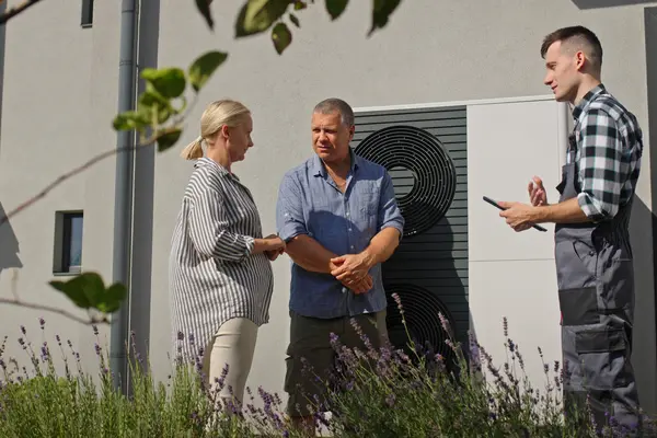 Energieberater mit einem Paar in einer Energieberatung an einer Wärmepumpe vor einem Wohnhaus