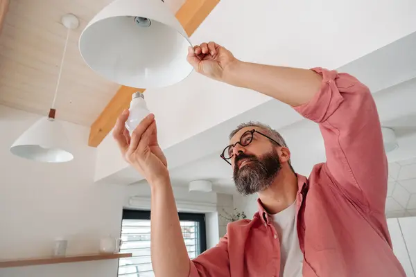 Mann schraubt Glühbirne in eine Lampe