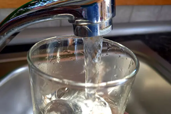 Aus einem Wasserhahn läuft Leitungswasser in ein Glas.