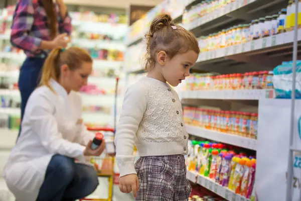 Ein Mädchen steht im Drogeriemarkt vor einem Regal mit Quetschies und anderen Kindersnacks