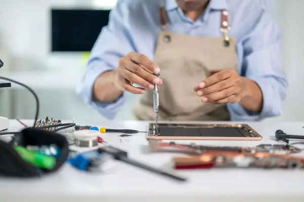 Ein Techniker repariert mit einem kleinen Schraubenzieher ein geöffnetes Tablet an einem Werkstatttisch voller Werkzeug.