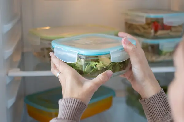 Eine Frau räumt Salat in einer Kühlbox in den Kühlschrank.