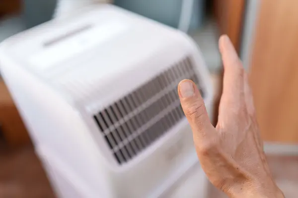Ein Mann hält seine Hand zum Kühlen an eine mobile Klimaanlage