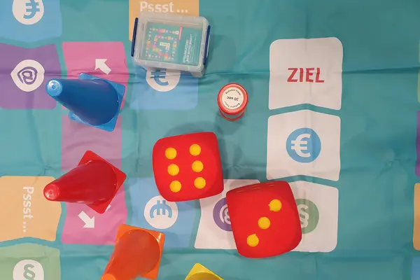 Verschiedenfarbige Spielfiguren und zwei Würfel, auf einem Spielfeld liegend 