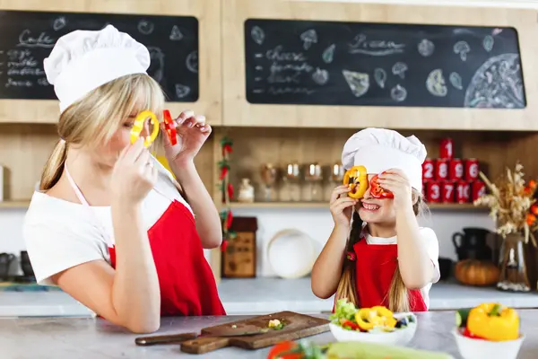 Zwei Personen mit Kochmütze stehen in der Küche und haben Paprikastücke in der Hand.