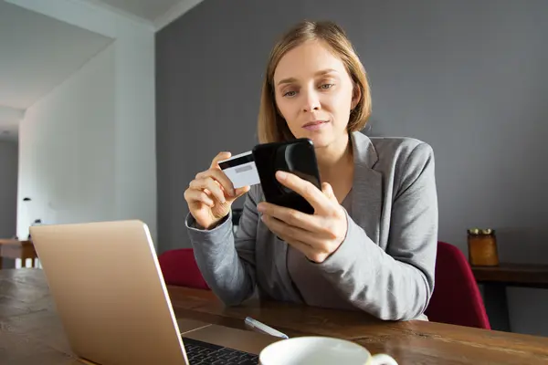 Eine junge Frau bezahlt etwas am Smartphone mit ihrer Bankkarte