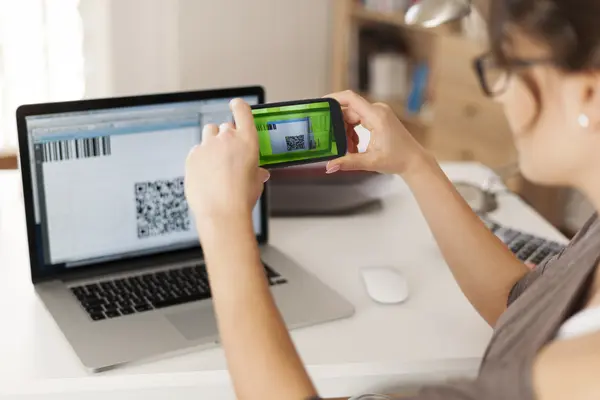 Eine Frau scannt mit ihrem Handy einen QR-Code am Laptop, um zu bezahlen