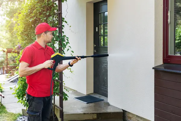 Mann reinigt eine Hausfassade mit einem Hochdruckreiniger