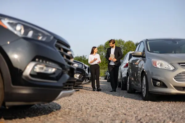 Frau und Gebrauchtwagenhändler zwischen Autos, die zum Verkauf stehen. Sonniges Wetter.