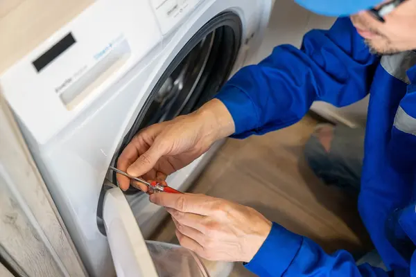 Ein Techniker repariert die Türdichtung einer Waschmaschine mit einem Schraubendreher.