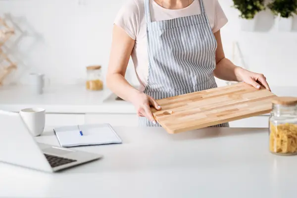 Frau bereitet sich auf Kochen vor, legt Brett auf Arbeitsplatte.