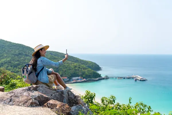 Frau nutzt Mobiltelefon im Urlaub auf Insel mit Berg