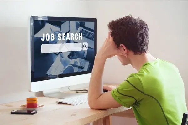 Mann sitzt am Schreibtisch, vor ihm ein großer Bildschirm mit der aufschrift Job search