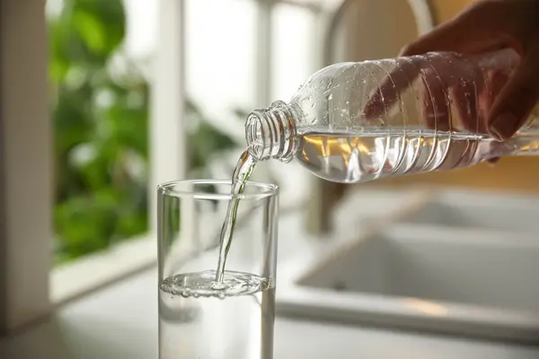 Nahaufnahme Person schenkt Wasser in Glas auf Arbeitsfläche in Küche