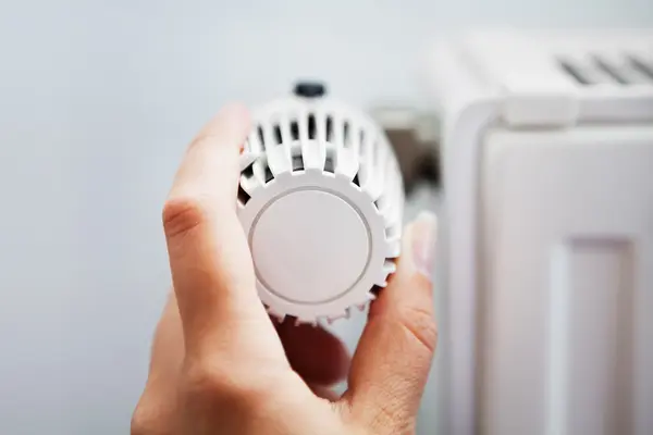 Eine Hand dreht den weißen Thermostatregler an einem Heizkörper.