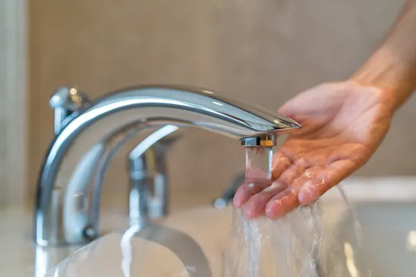 Eine Hand wird unter fließendes Wasser aus einem verchromten Wasserhahn gehalten.