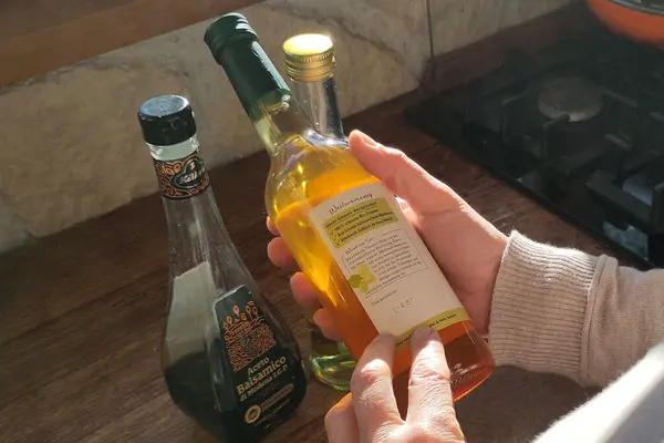 Eine Person betrachtet das Etikett auf der Rückseite einer Essigflasche. 