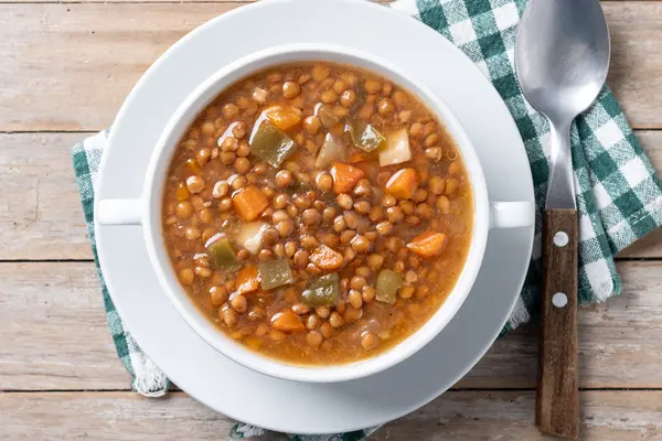 Ein Teller mit Linsensuppe, rechts davon ein Esslöffel auf einer grün-weiß karierten Serviette