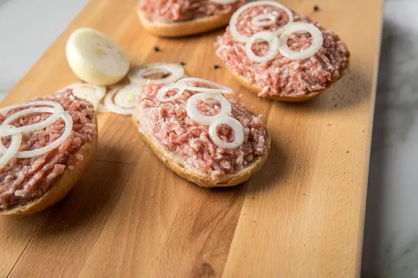 Vier Mettbrötchen mit Zwiebelringen liegen auf einem Holzbrett.