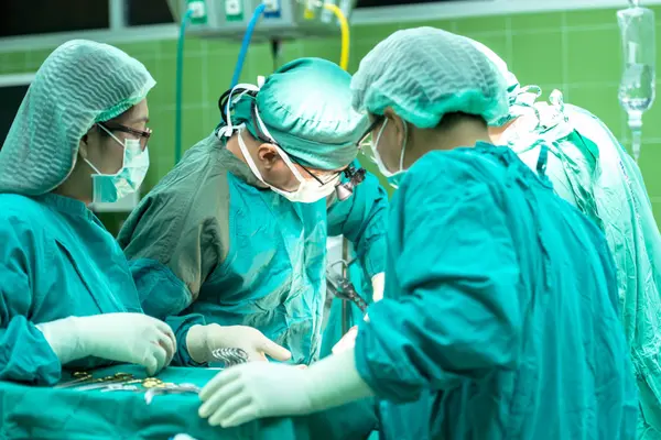 Blick in einen Operationssaal im Krankenhaus mit drei Personen in grüner Schutzkleidung während einer Operation