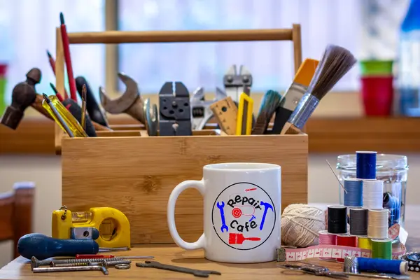 Ein Werkzeugkasten steht neben Näh-Utensilien und einem Kaffeebecher mit der Aufschrift "Repair-Café". 