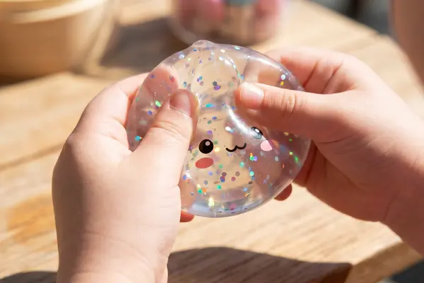 Kinderhände drücken ein Quetschspielzeug, genannt Squishy, das eine klare Flüssigkeit mit Glitzer enthält.