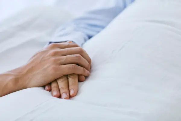 eine Person legt ihre Hand auf die einer im Krankenhausbett liegenden weiteren Person