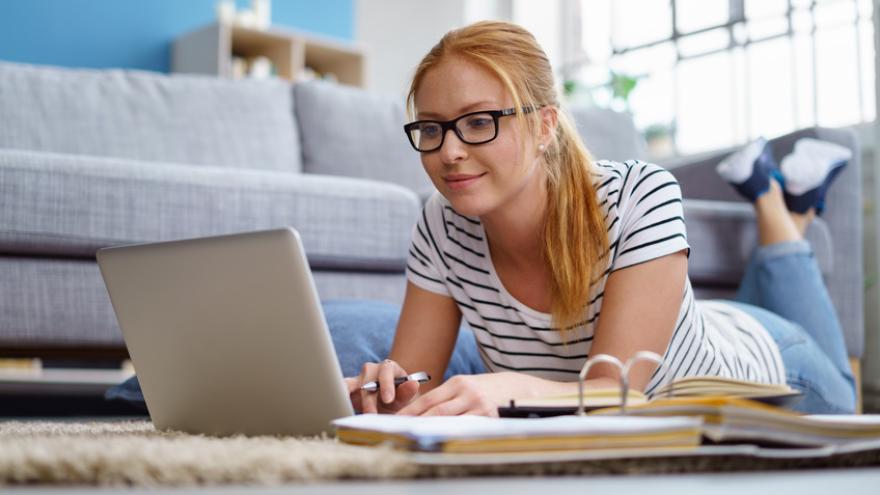 Junge Frau liegt am Boden und surft im Laptop nach Auktionsportalen für Zahnersatz