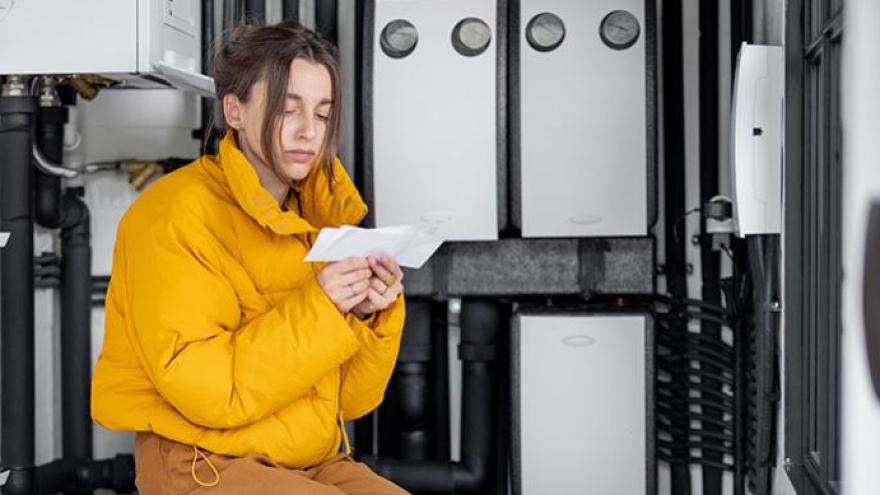 Frau sitzt in einem Heizungskeller und schaut entsetzt auf eine Rechnung