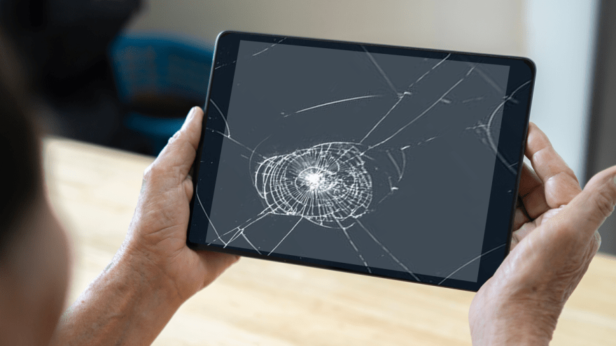 Ältere Hände halten ein Tablet mit einem gesprungenem Display.