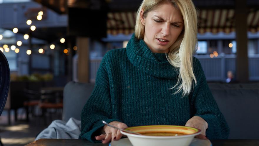 Eine Frau schaut angeekelt auf einen Teller mit offenbar verdorbenem Essen.