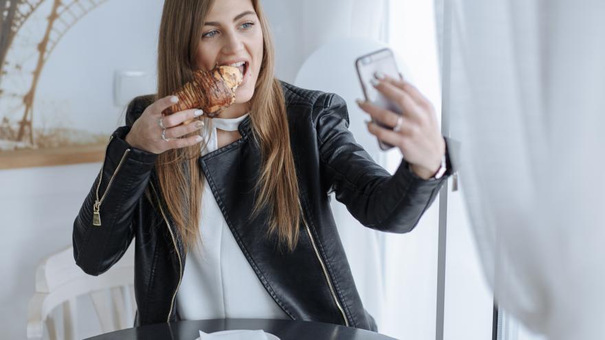 Ein Influencerin filmt sich, wie sie ein Croissant isst