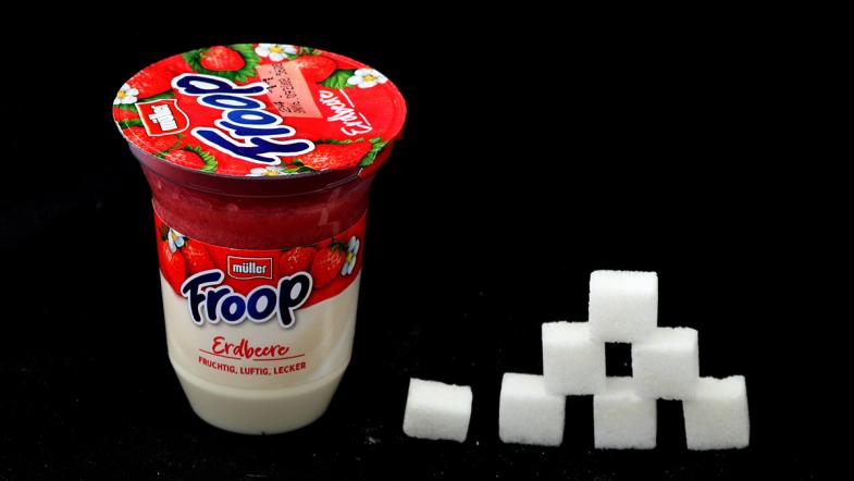 Joghurtbecher von Müller Froop und daneben eine Zuckerwürfel-Pyramide