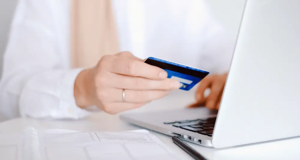 Person sitzt mit Kreditkarte am Laptop