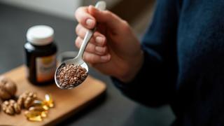 Hand hält Löffel mit Leinsamen in der Nähe von Nahrungsergänzungsmitteln