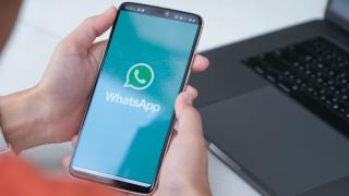 Jemand hält ein Handy in der Hand, auf dessen Display das WhatsApp-Logo zu sehen ist