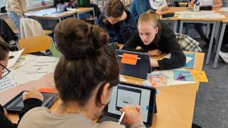 Junge Personen arbeiten an Tablets an einem Gruppentisch.